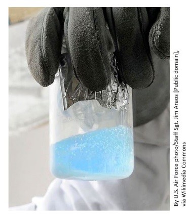 Gloved hand holding beaker of pale blue liquid