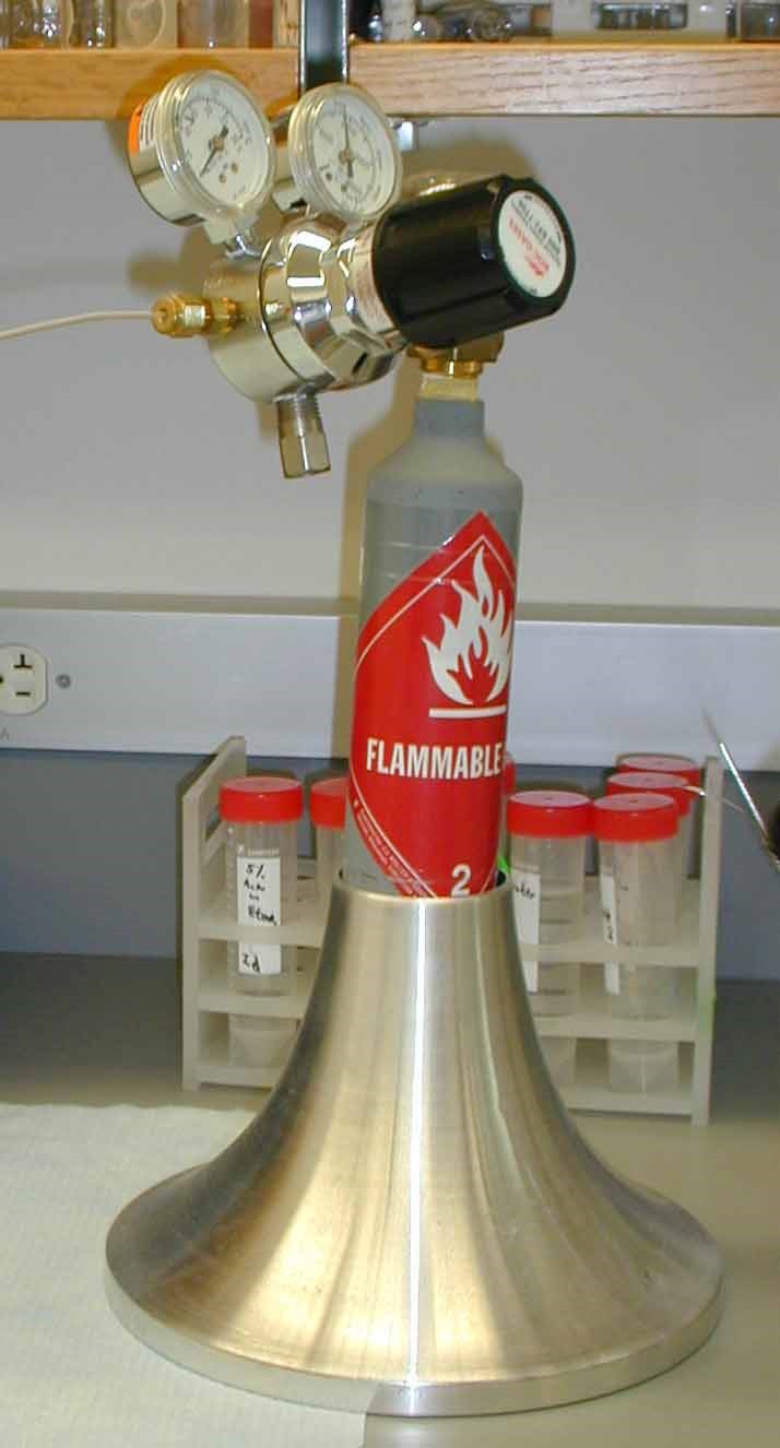 A small gas cylinder in an upright stand with flared bottom