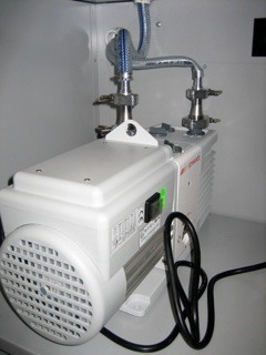 Vacuum pump in vacuum cabinet with exhaust vented through cabinet wall into fume hood